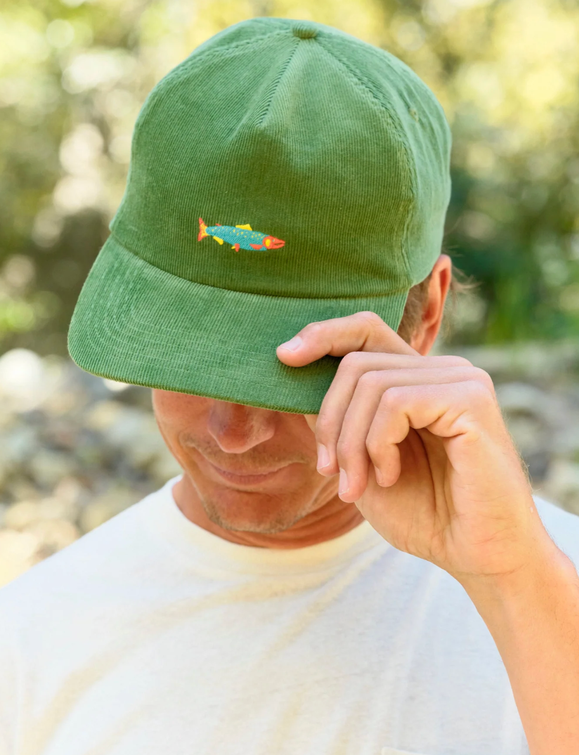 Person wearing a green cap with a colorful fish emblem, outdoors.