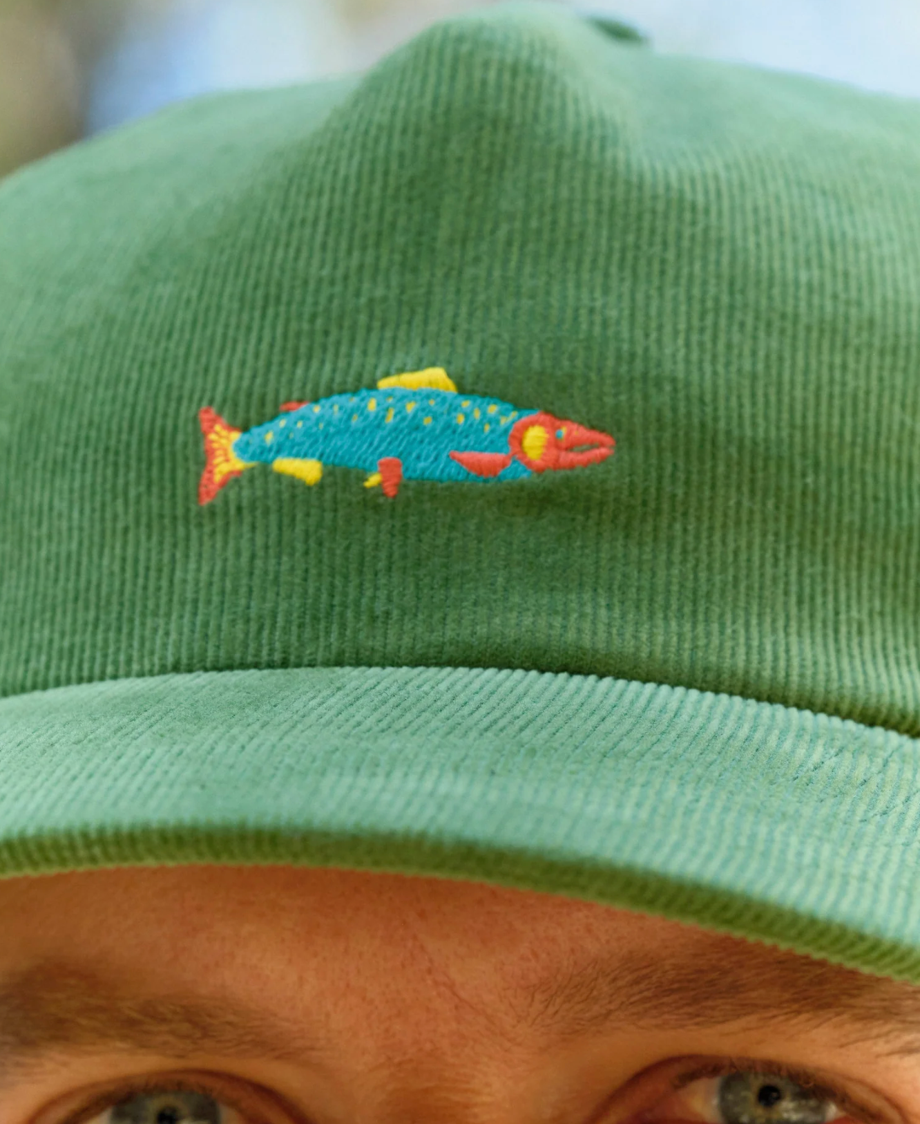 Green cap with a colorful fish design worn by a person.
