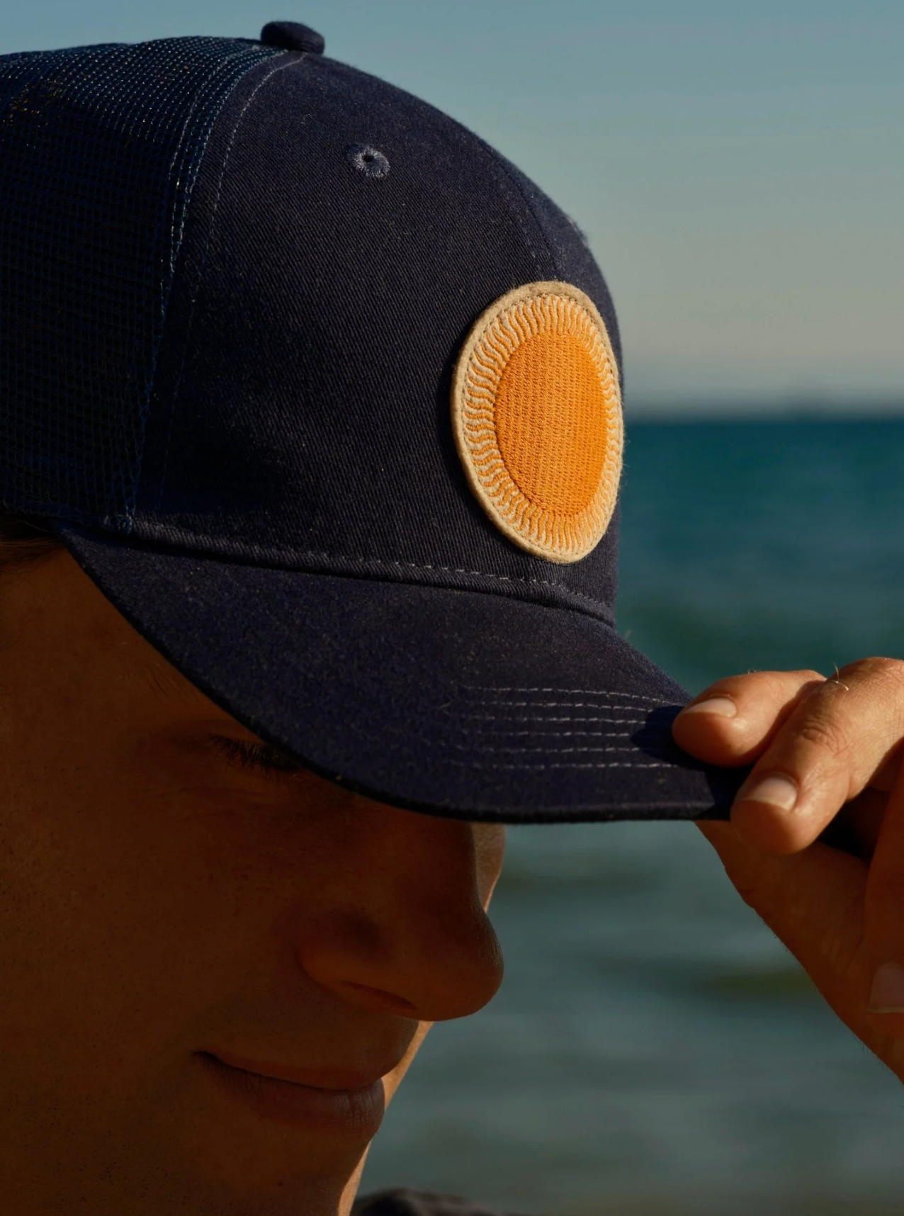 Person wearing a navy blue cap with a yellow patch against a blurred natural background