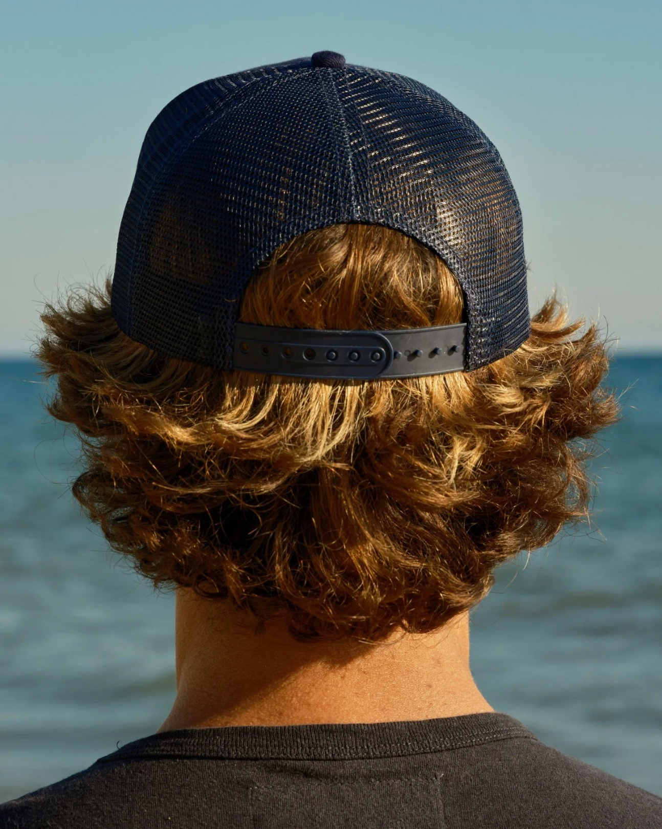 Person wearing a navy blue mesh cap with a blurred ocean background