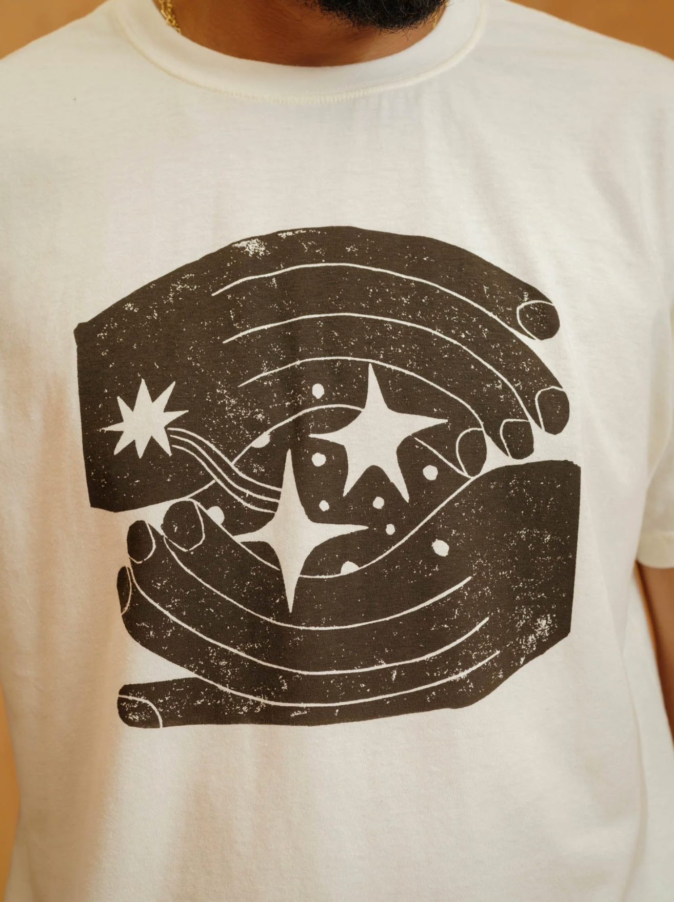 White t-shirt with a black graphic design of a hand holding stars on a plain background