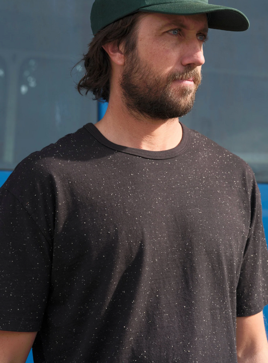 Man wearing a black t-shirt and green cap against a blue background