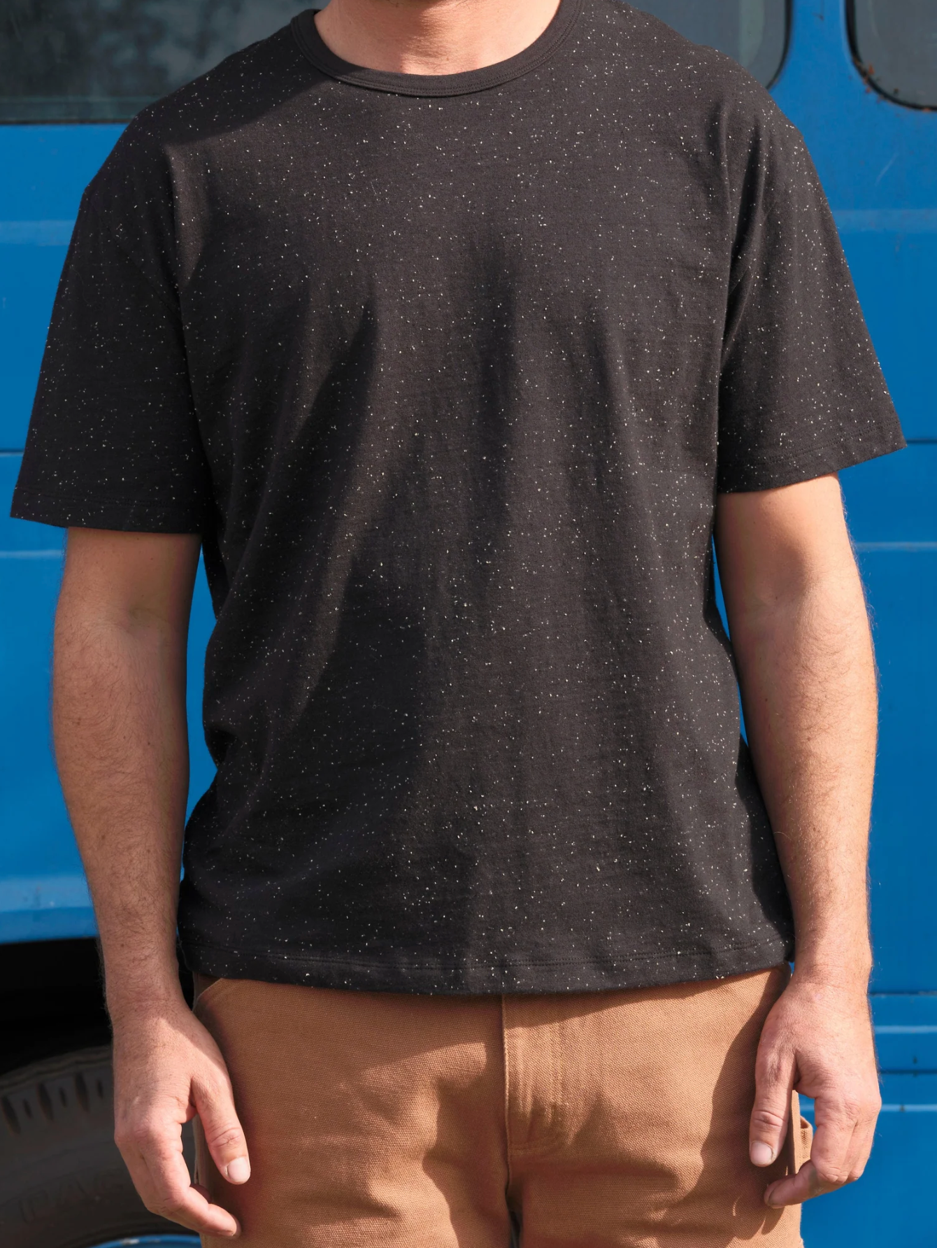 Person wearing a black t-shirt with a blue vehicle in the background