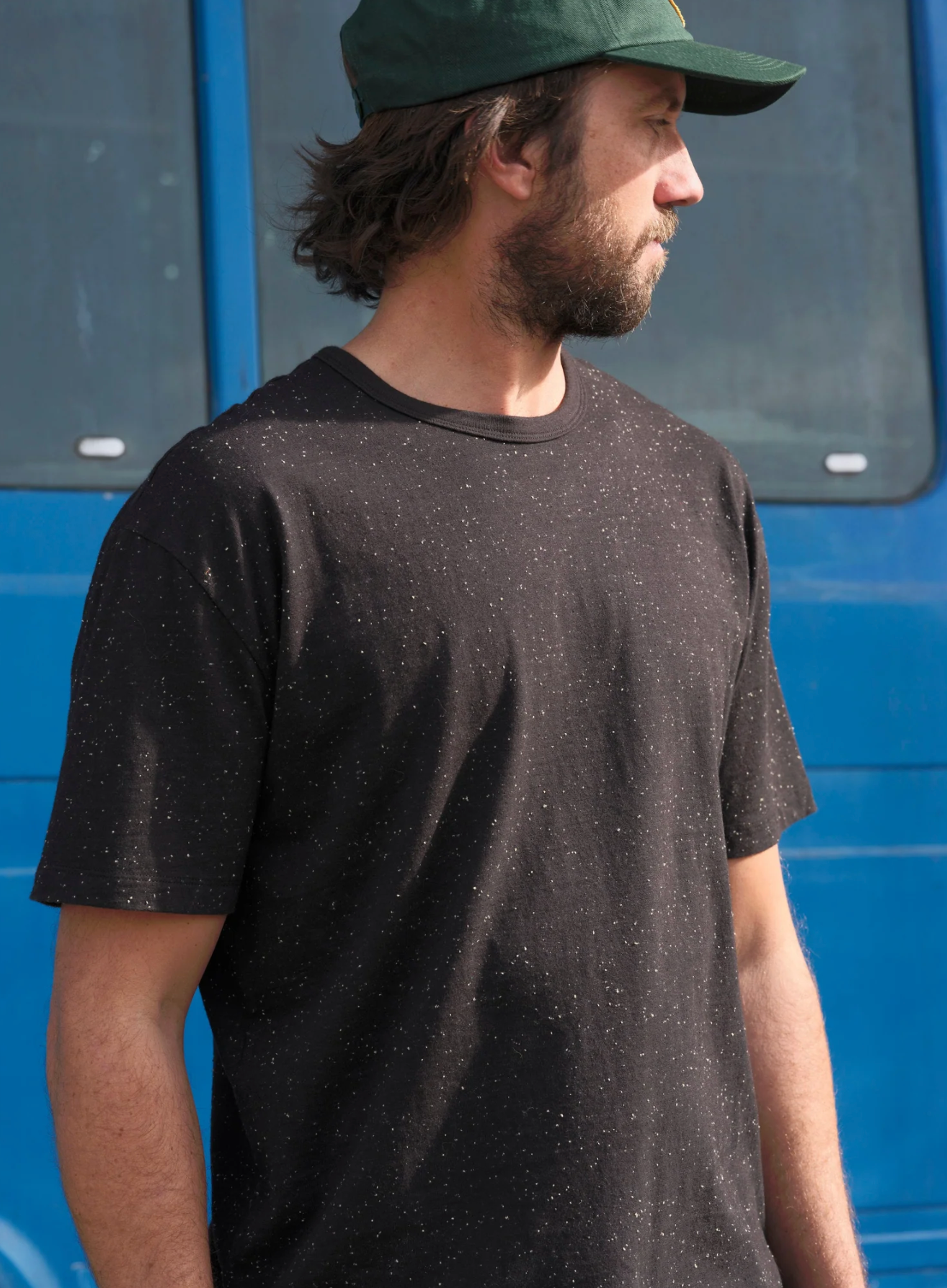 Man wearing a dark t-shirt and green cap standing in front of a blue vehicle.