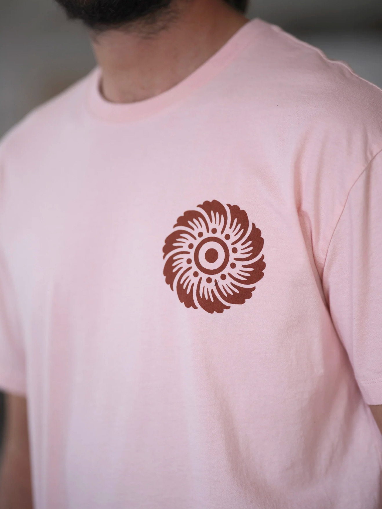 Person wearing a light pink t-shirt with a brown circular design on the chest.