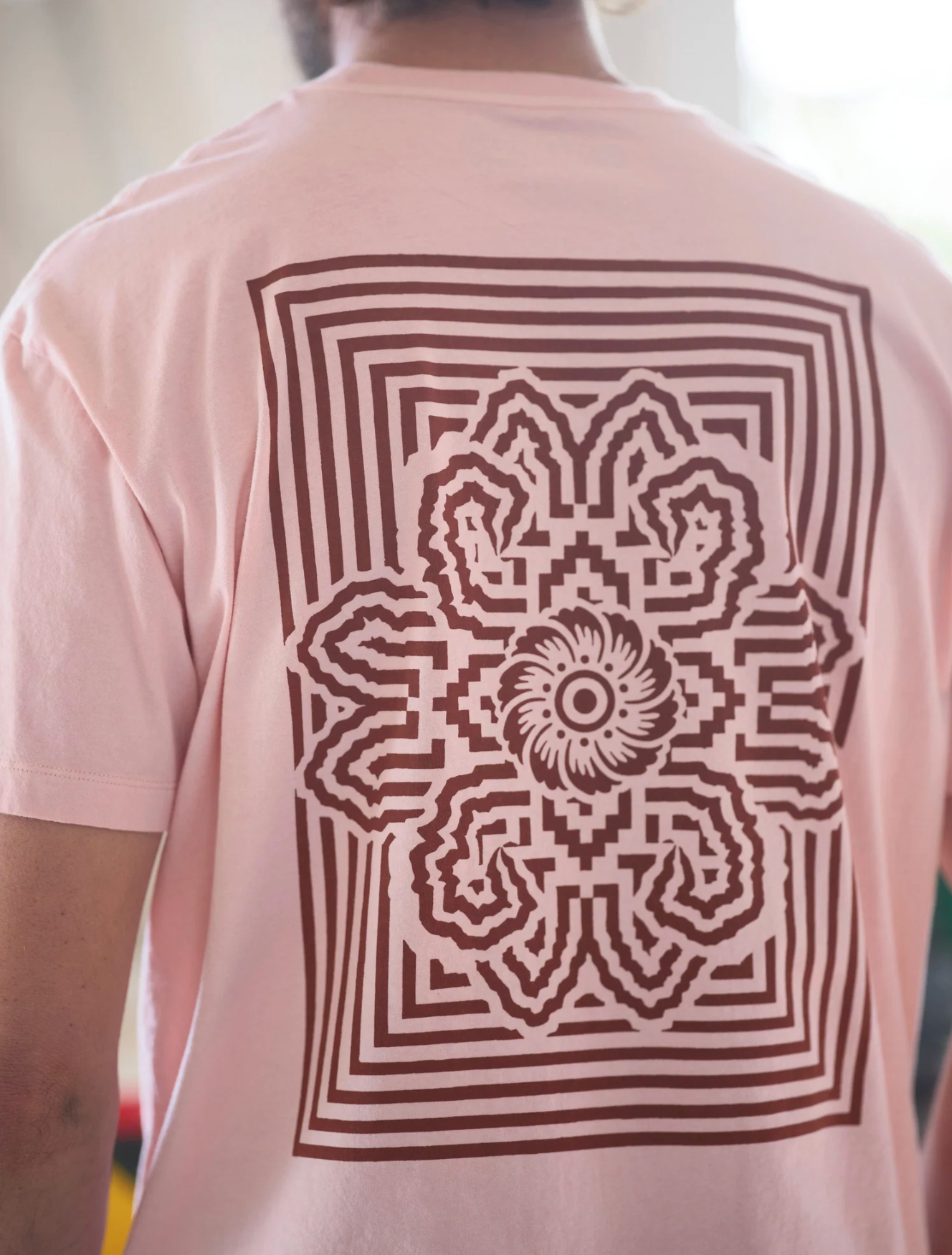 Person wearing a pink t-shirt with a brown geometric floral design on the back.