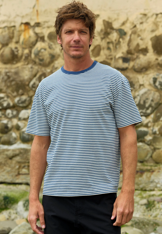 Man wearing a striped shirt standing in front of a stone wall.