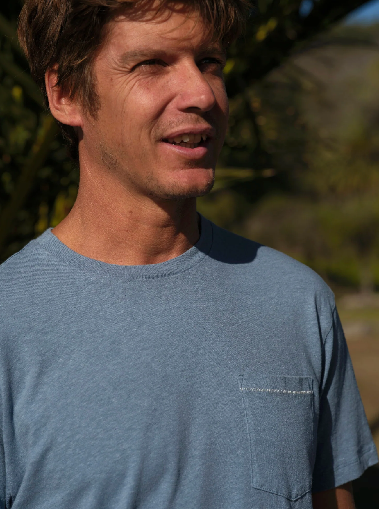 Man wearing a blue t-shirt outdoors with a blurred natural background