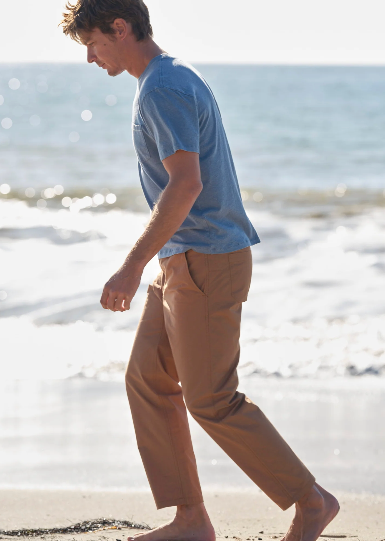 Man walking on a beach wearing a blue shirt and beige pants.