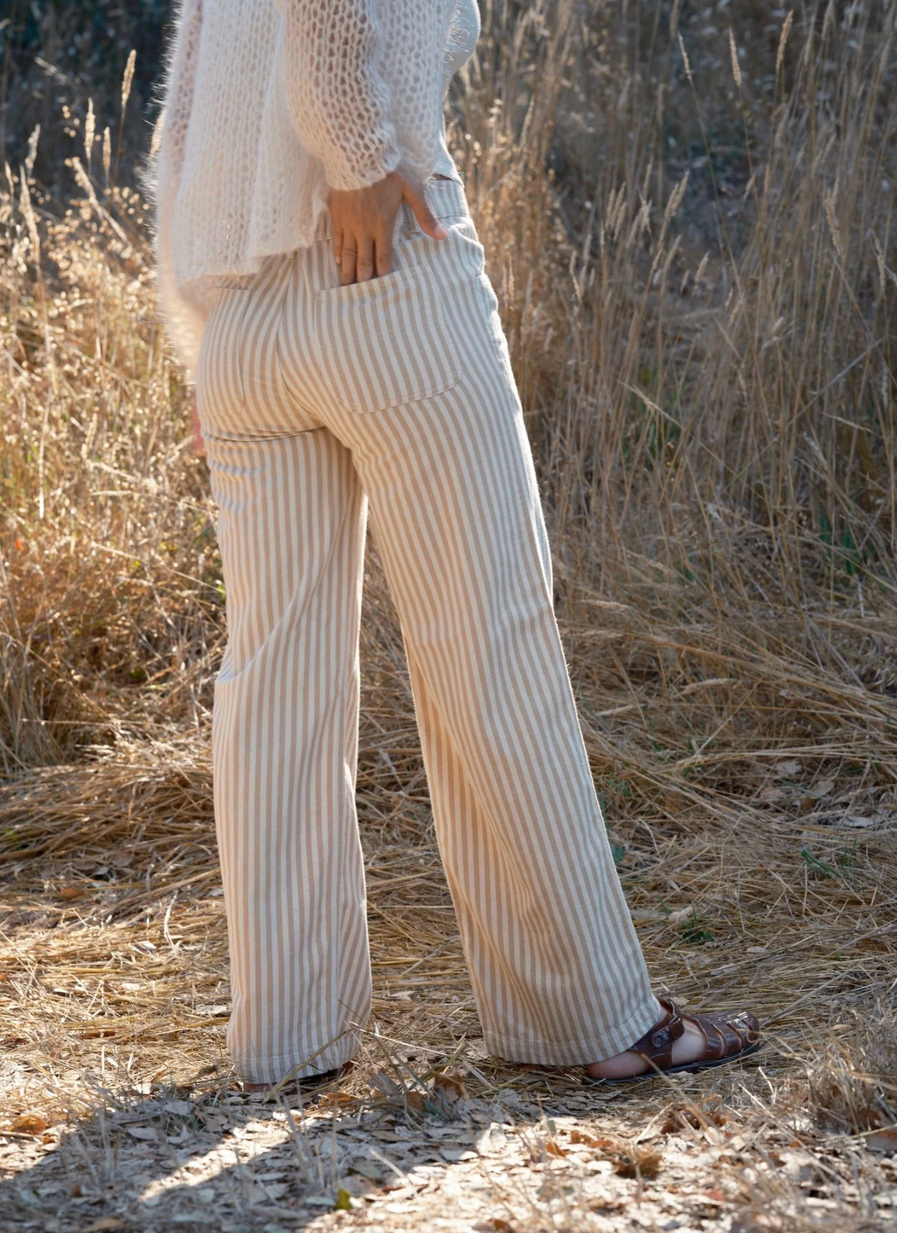 Person wearing a cream ribbed sweater and pants standing in a natural setting with dry grass.