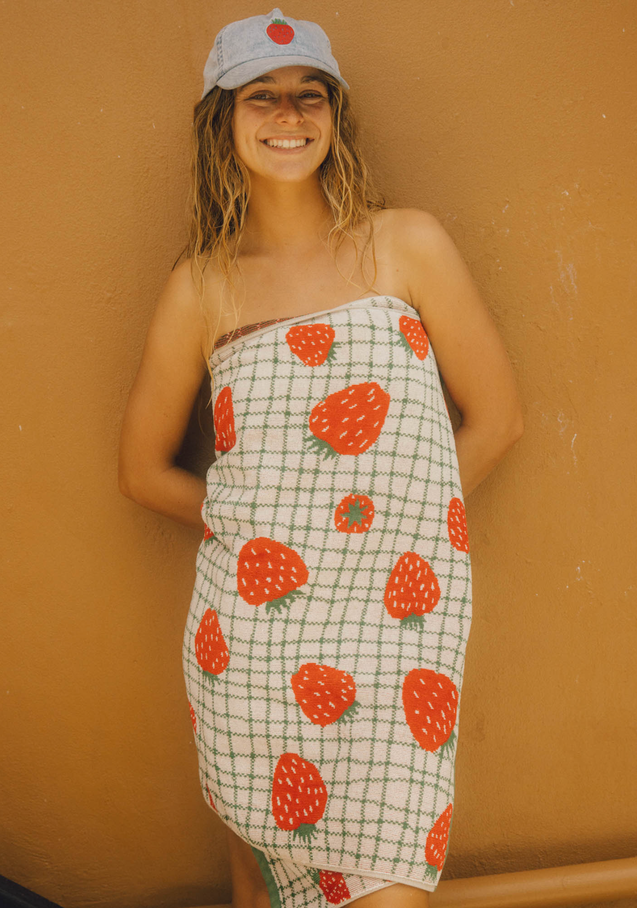 Person wearing a strawberry-patterned dress and cap against a beige wall