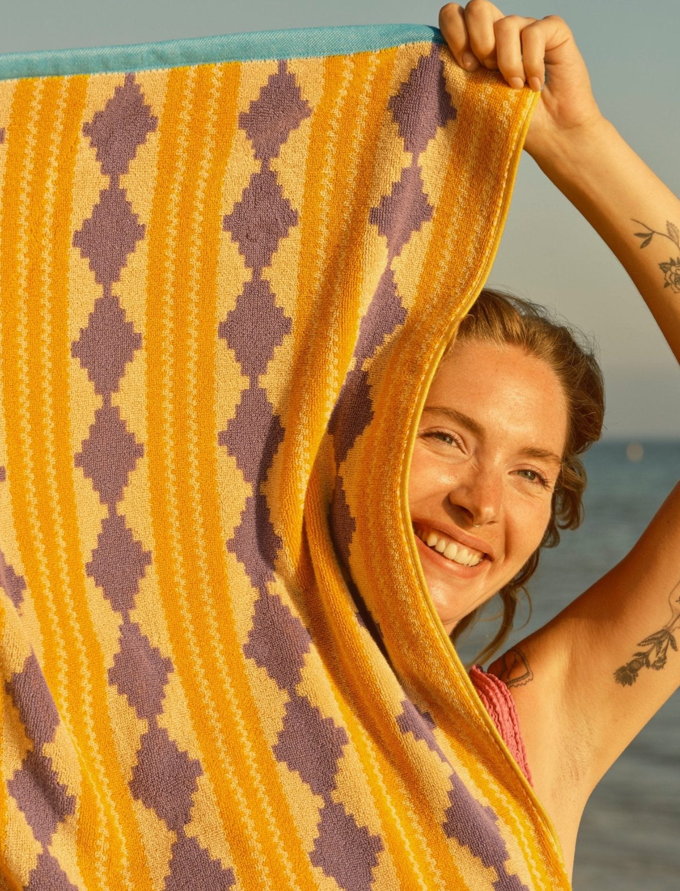 Woman holding a yellow and purple patterned towel with ocean in the background