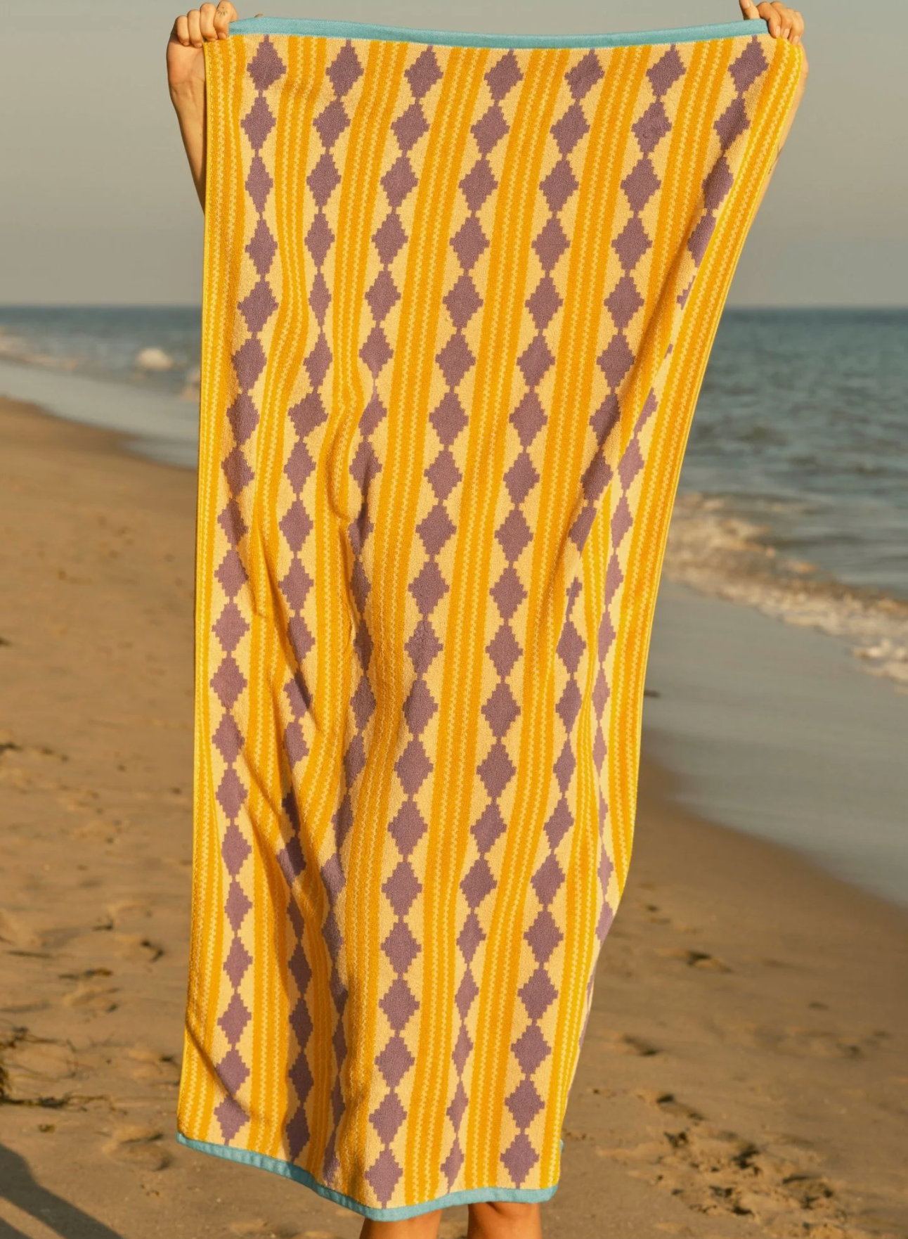 Person holding a yellow and brown patterned towel on a beach