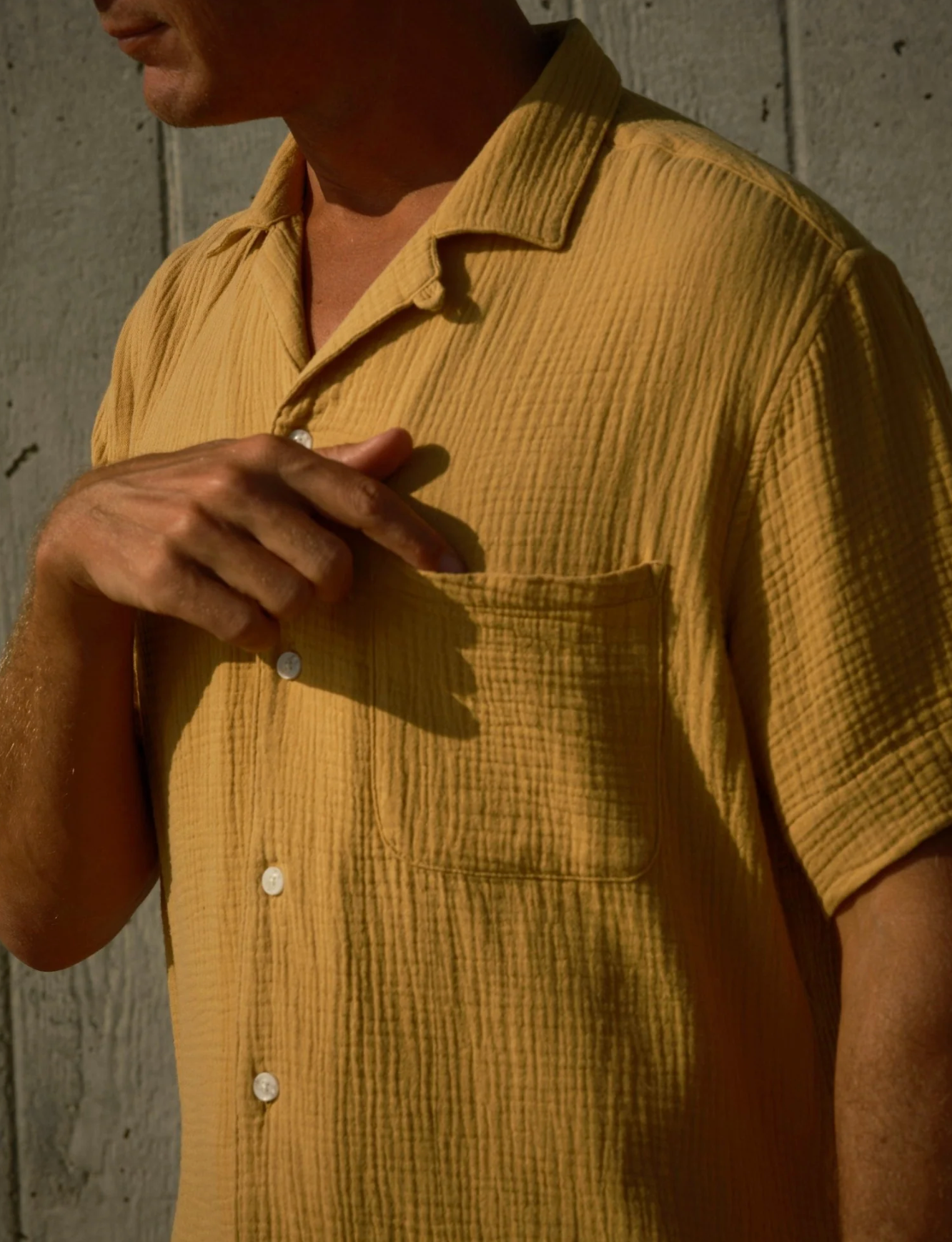 Close-up of a person wearing a mustard yellow textured shirt against a concrete wall.