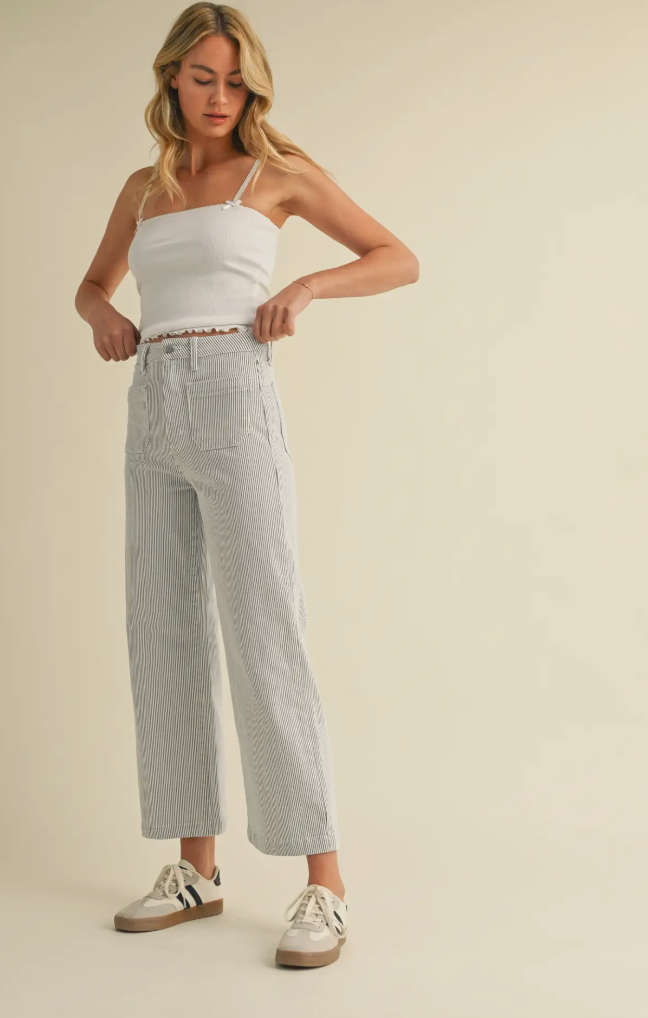 Woman wearing a white tank top and light gray pants on a beige background