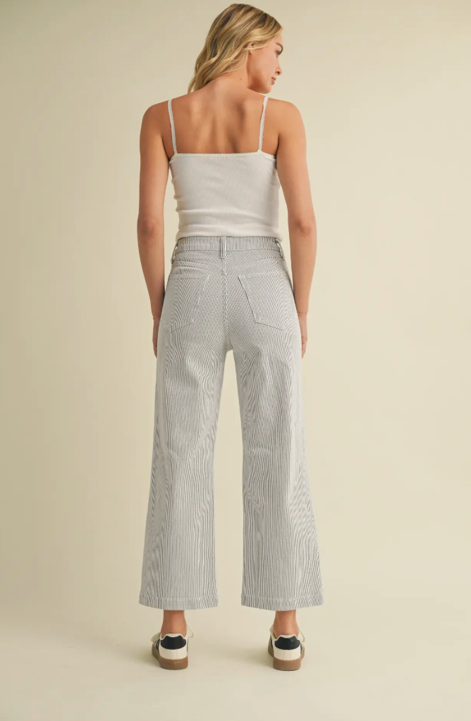 Woman wearing a light gray tank top and wide-leg pants on a beige background