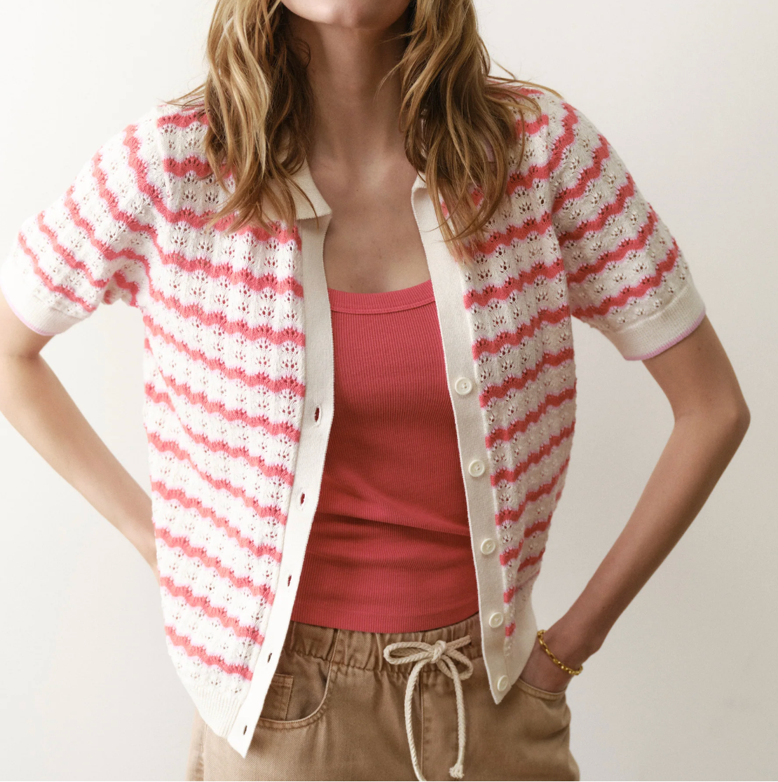Woman wearing a red and white striped cardigan over a pink top against a plain background