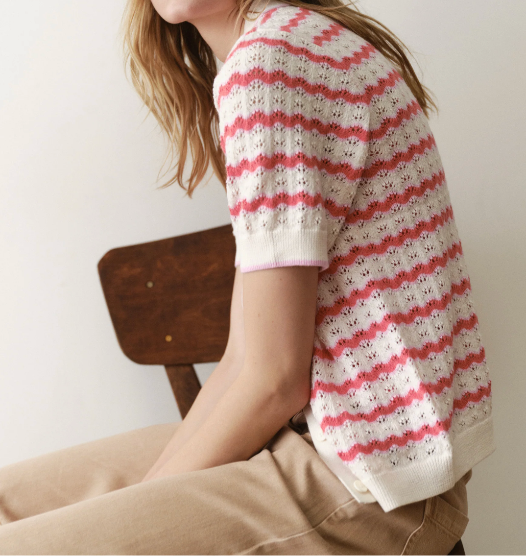 Woman wearing a red and white striped sweater sitting on a wooden chair against a white wall.
