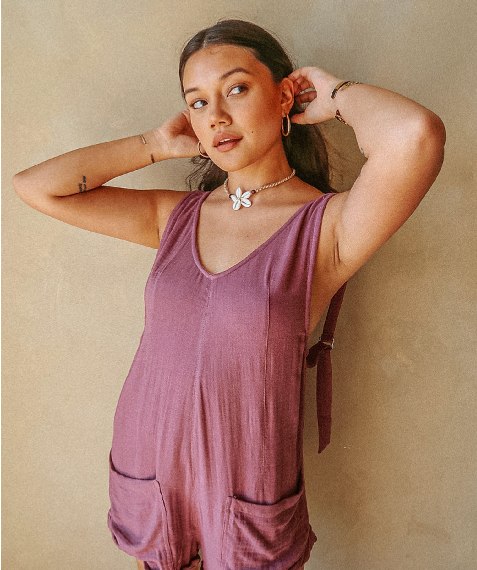 A person wears purple lineny romper against a beige background. 
