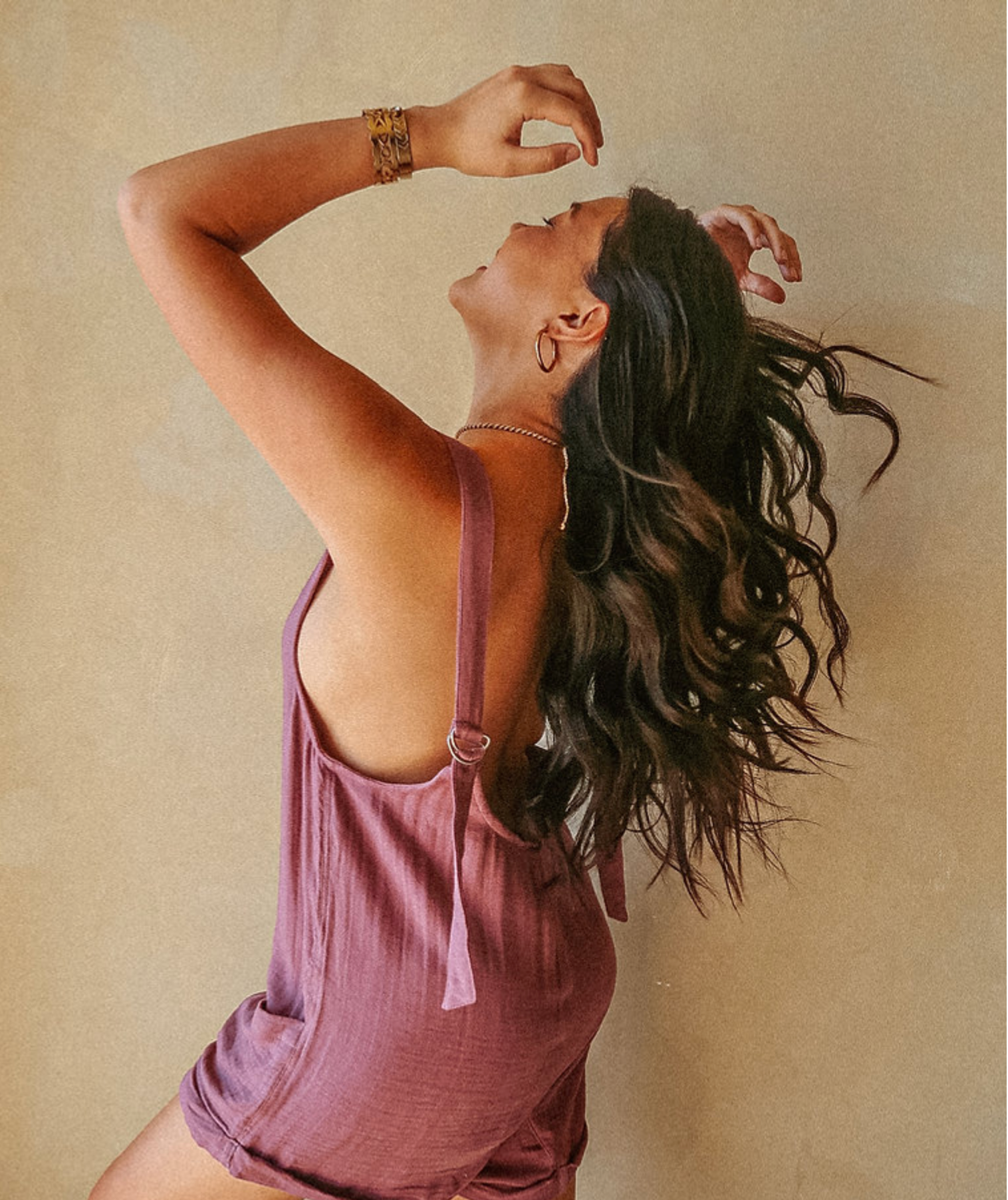 A person showcases the back of a purple romper against a beige background.