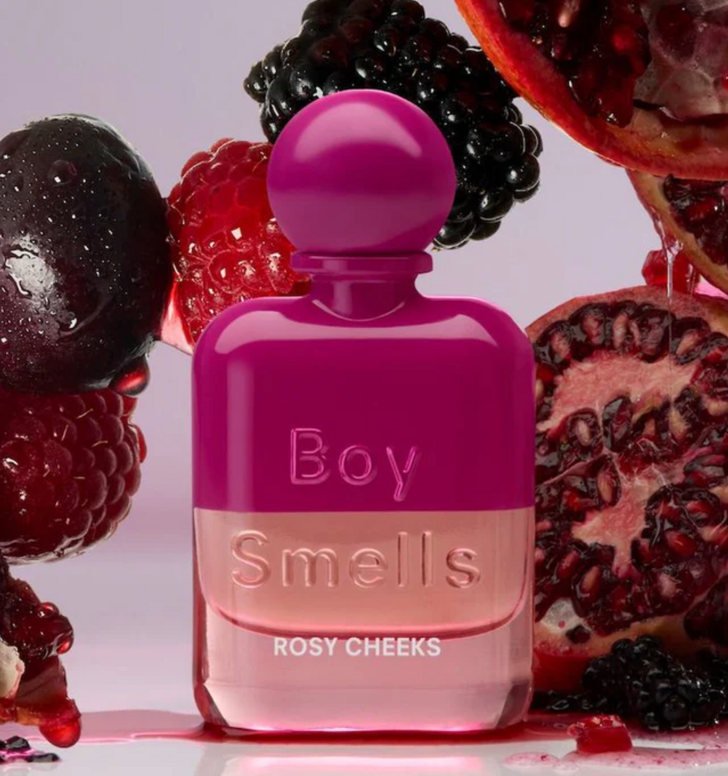 Pink perfume bottle labeled 'Boy Smells Rosy Cheeks' surrounded by berries on a light pink background