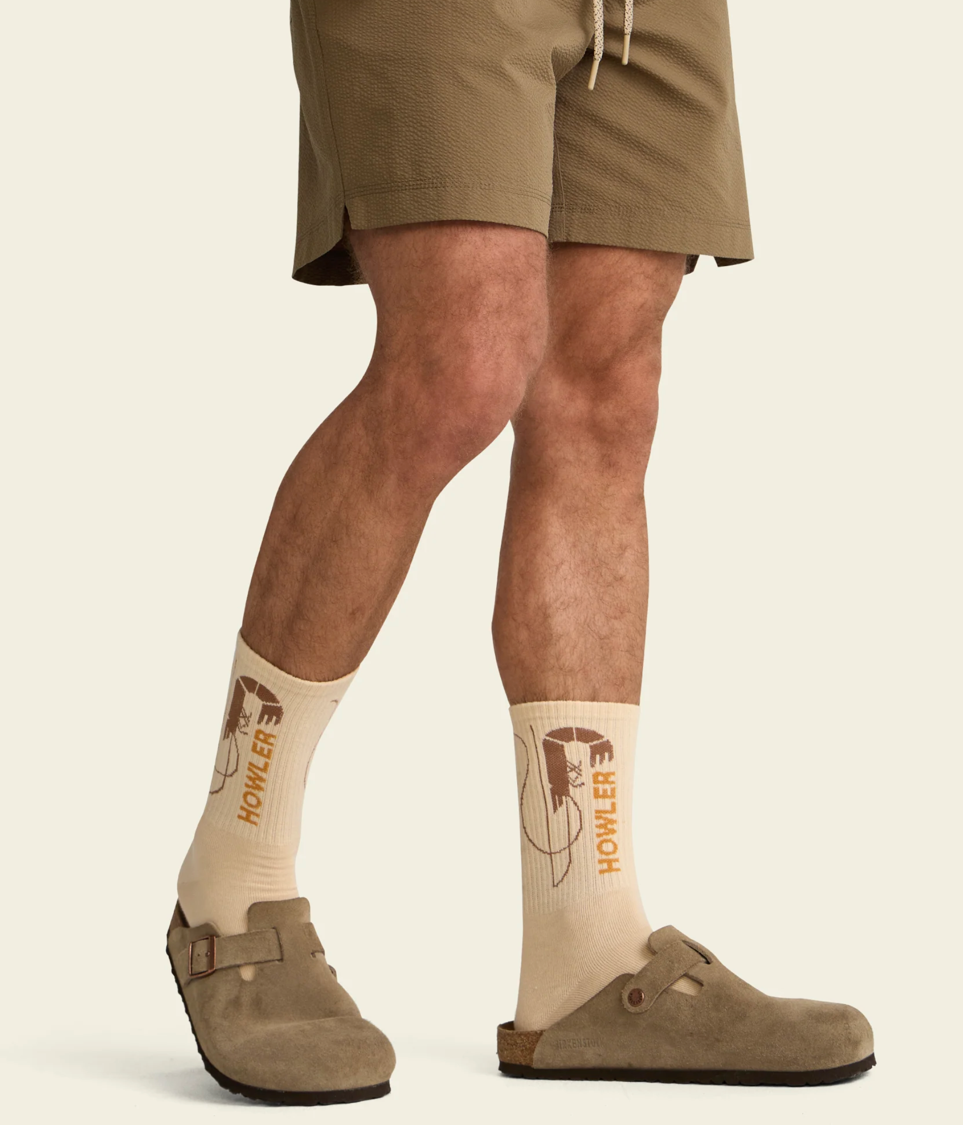 Person wearing khaki shorts and socks with a logo on a beige background