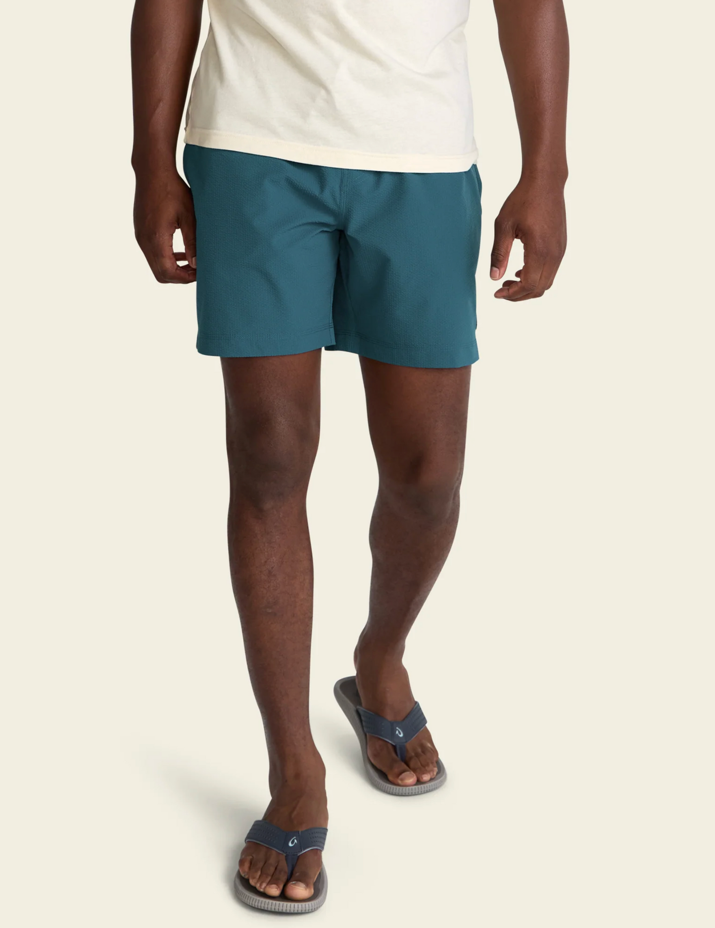 Person wearing blue shorts and sandals on a beige background