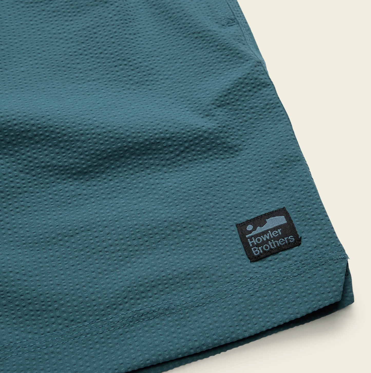 Close-up of a teal fabric with a Howler Brothers logo on a light gray background