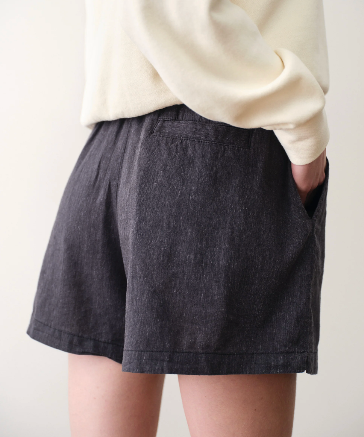 Person wearing dark denim shorts and a cream sweater on a plain background