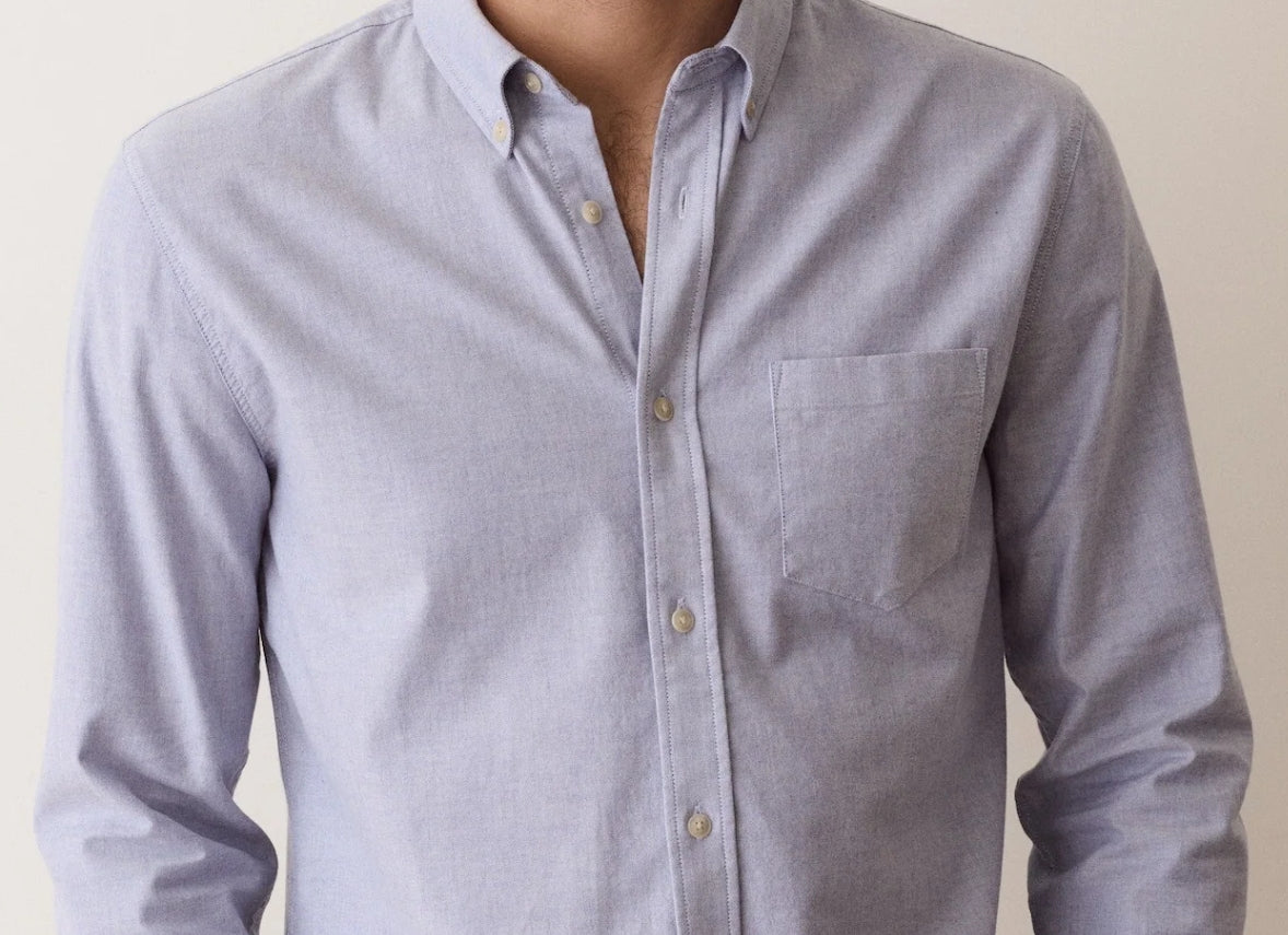 A man wearing a light blue long-sleeve button-down shirt with a chest pocket, shown from the neck down against a plain light background.