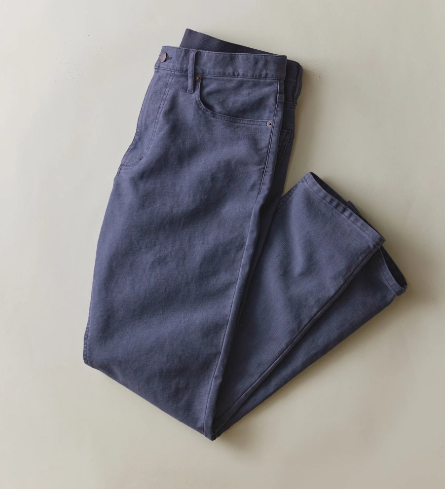 A pair of folded blue-gray chino pants laid flat on a light beige background.