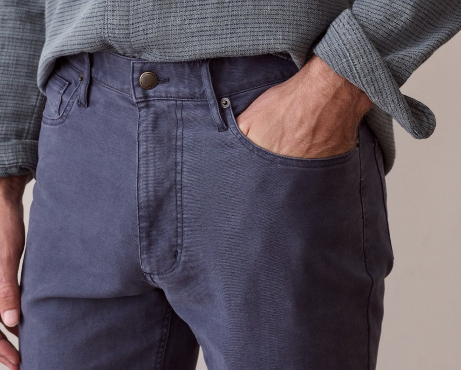 Close-up of a person wearing dark slate blue denim jeans with a gray ribbed knit shirt tucked in, showing the front pocket and waistband.