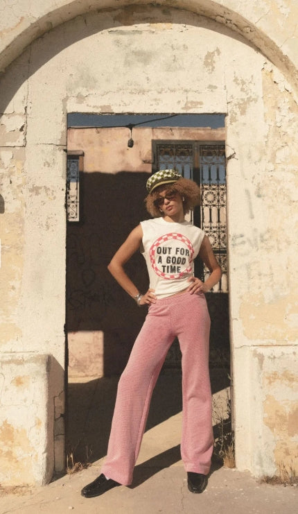 Person wearing a white t-shirt with text and pink pants standing in front of a stone archway.