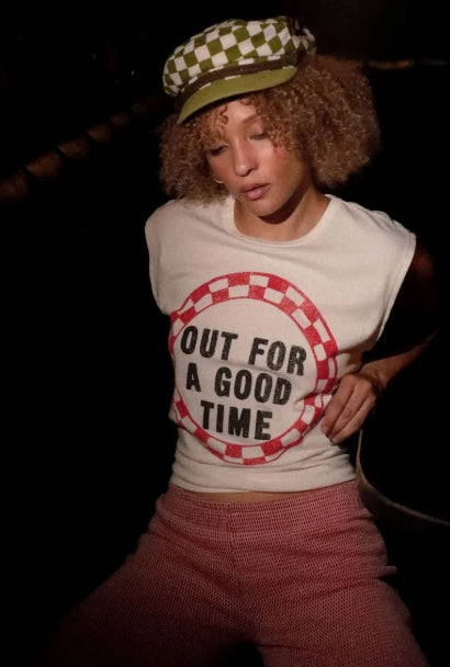 Person wearing a sleeveless shirt with 'Out for a Good Time' text and a checkered cap.