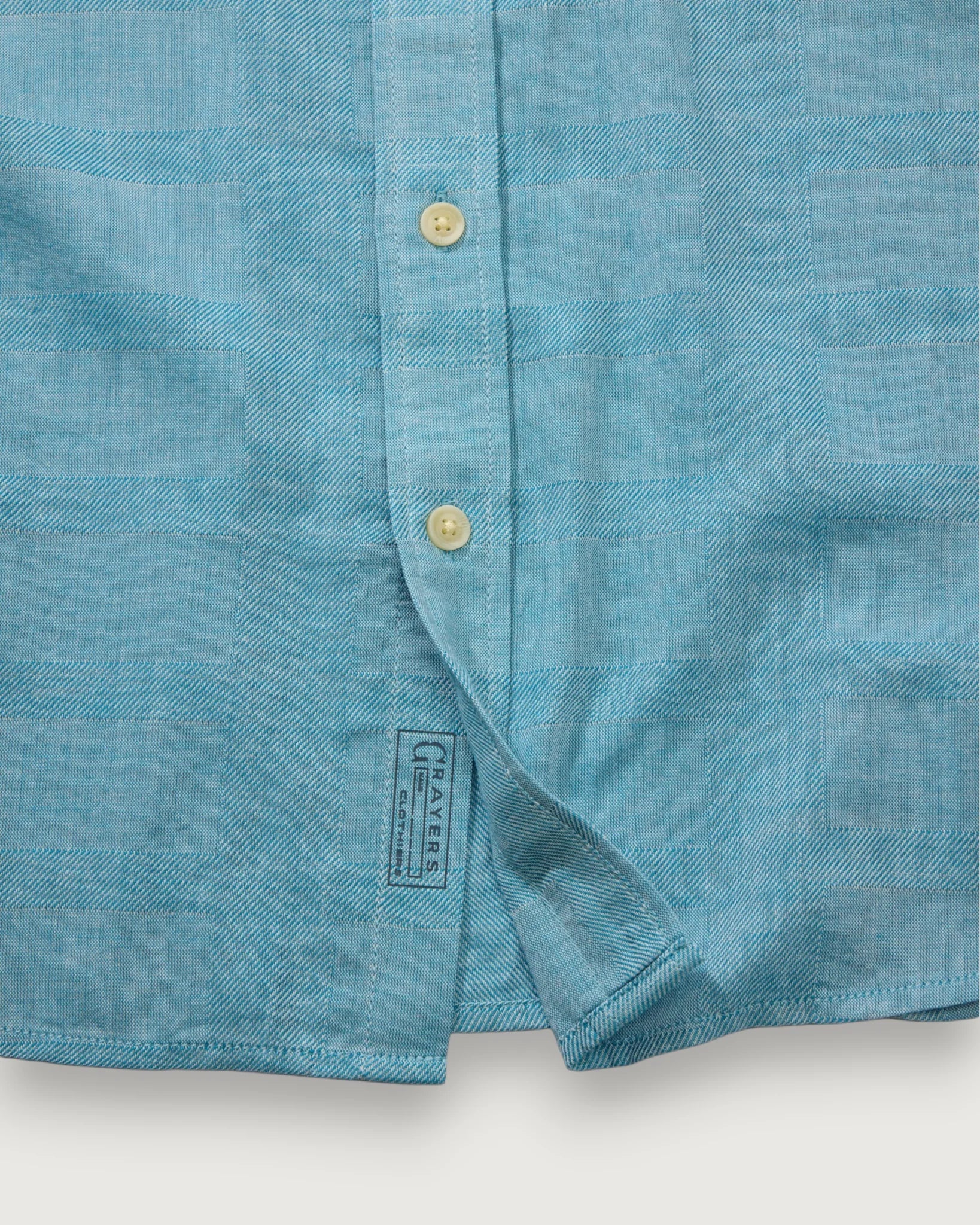 Close-up of a blue shirt with buttons and a brand label on a white background