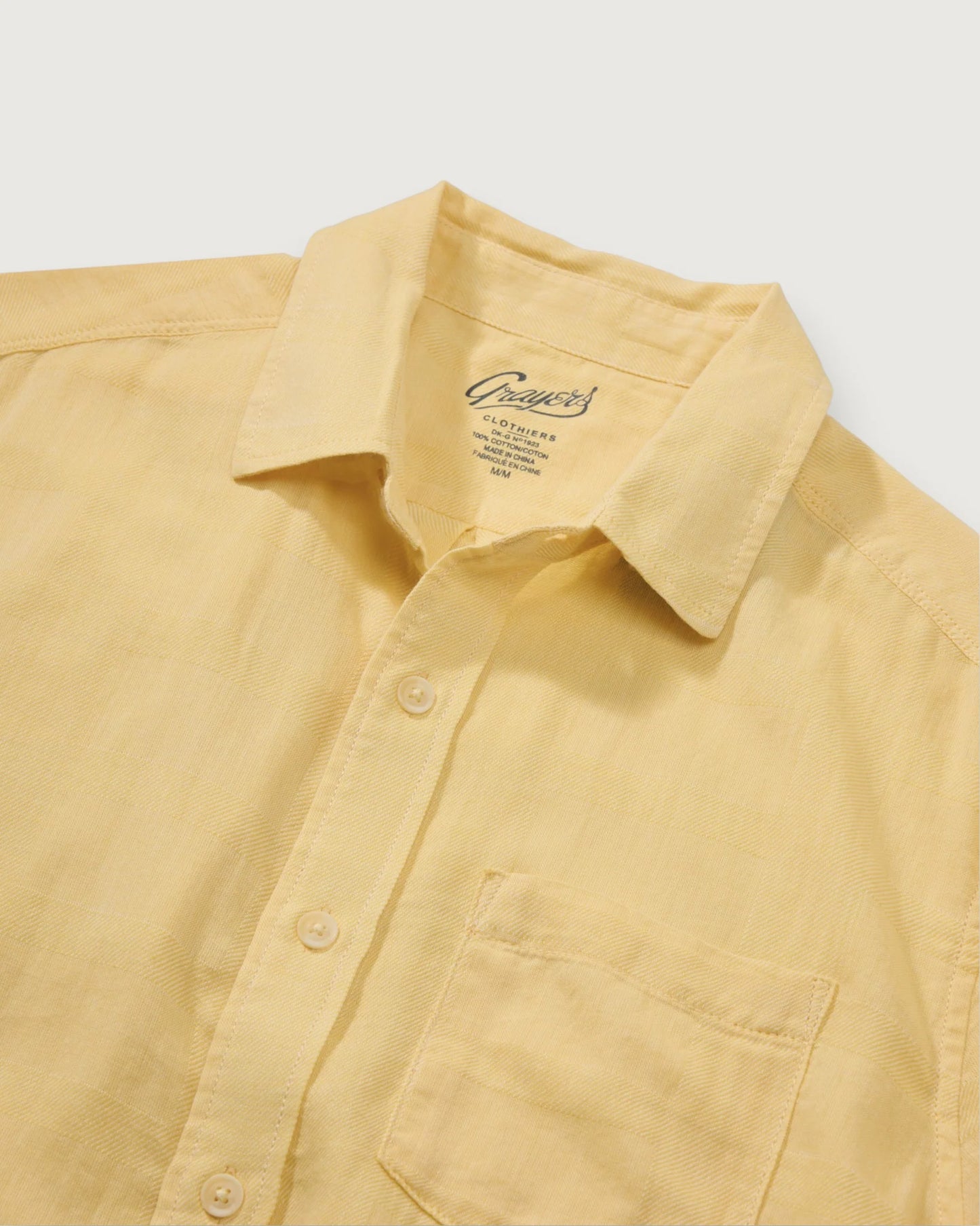 Yellow shirt with collar and brand logo on a light gray background