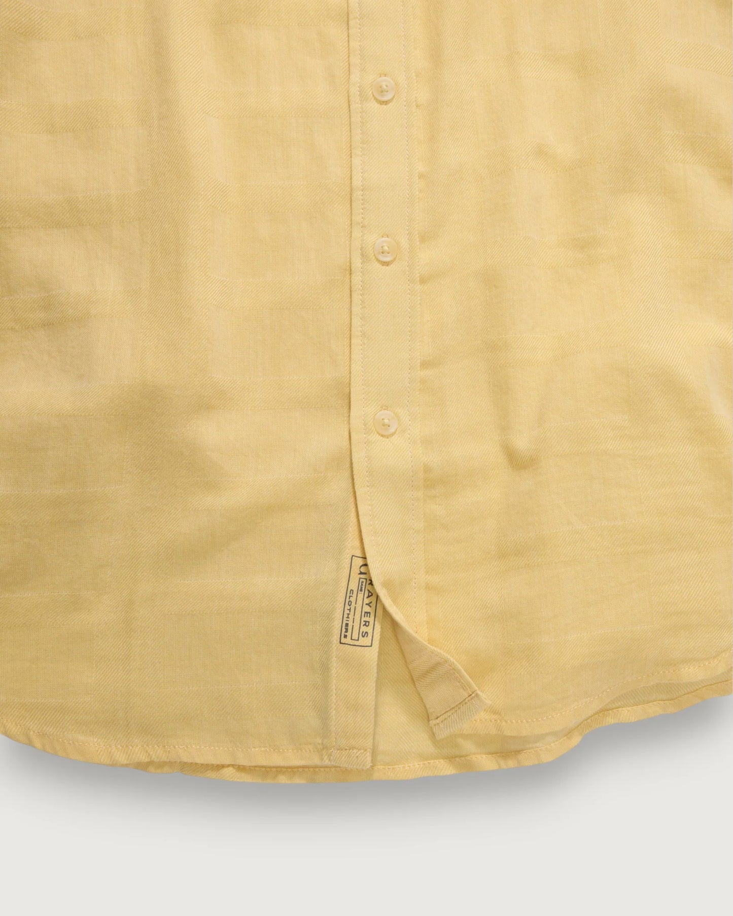 Close-up of a mustard yellow shirt with a brand label on a light gray background