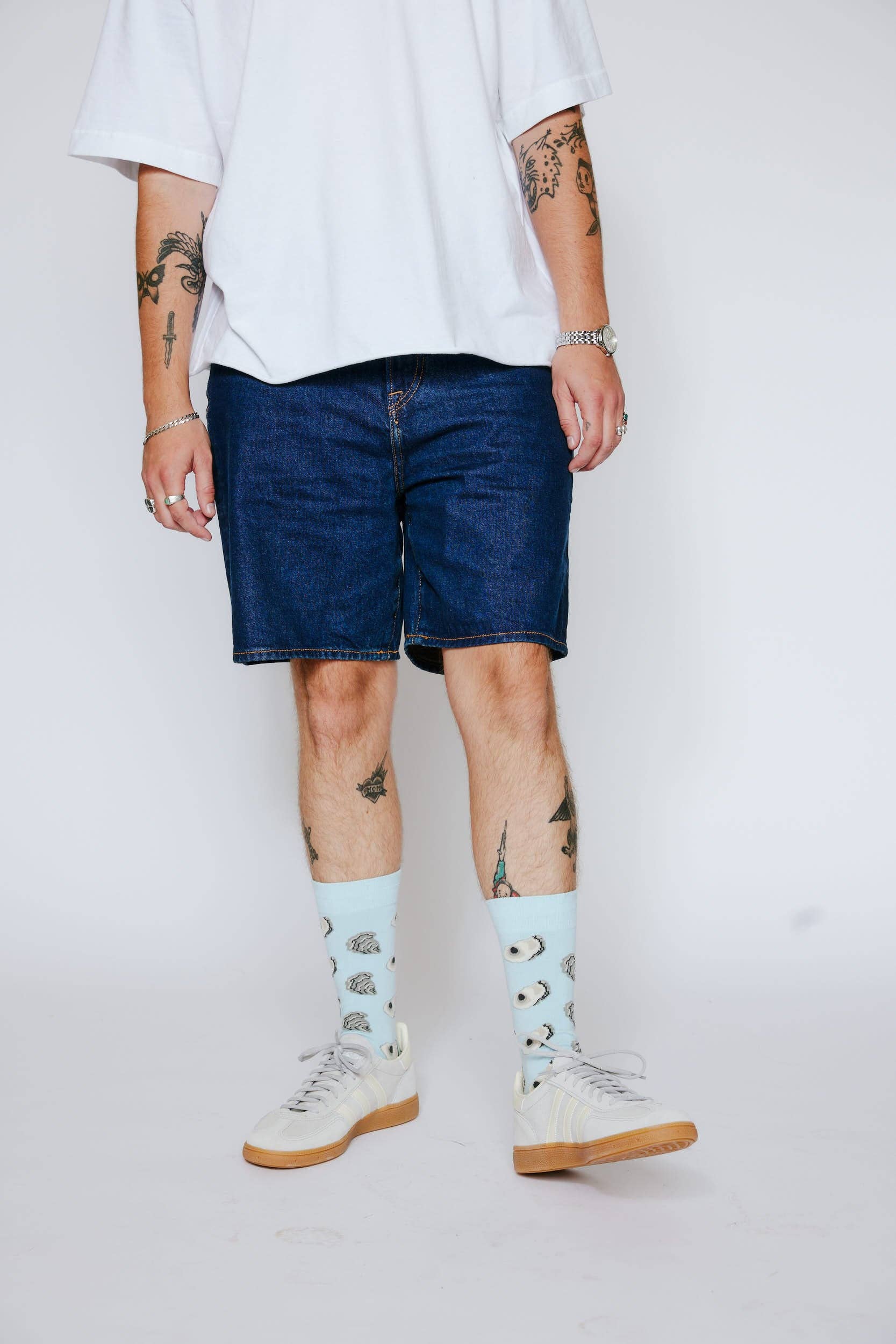 Person wearing a white t-shirt, blue denim shorts, and light blue socks with a pattern on a plain background.