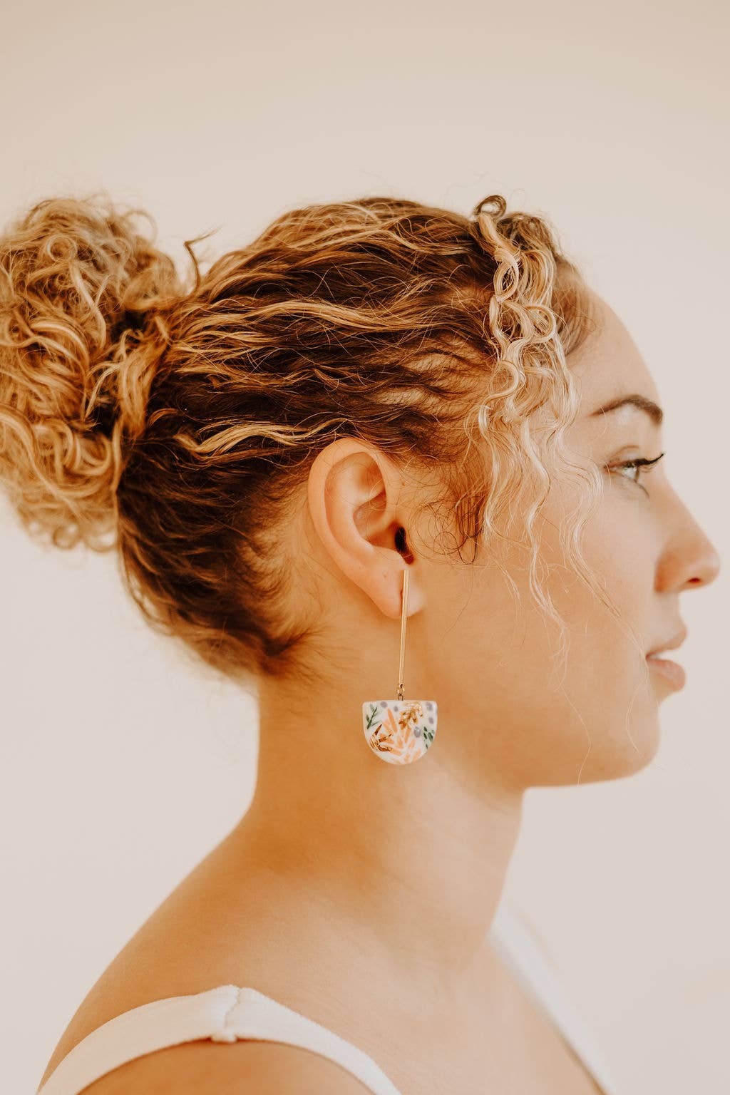 Side profile of a woman wearing floral hoop earrings against a neutral background