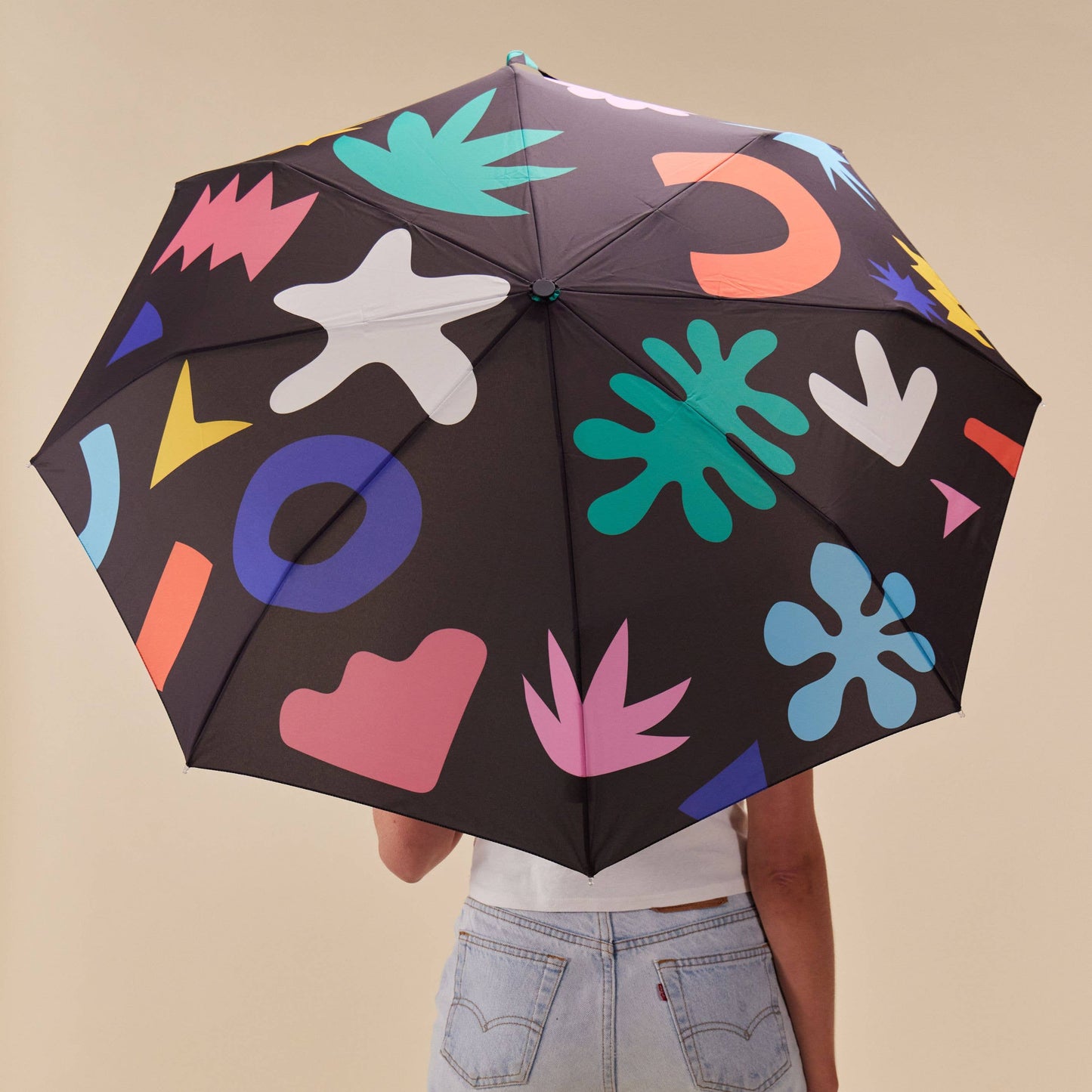 Person holding a black umbrella with colorful abstract patterns on a beige background