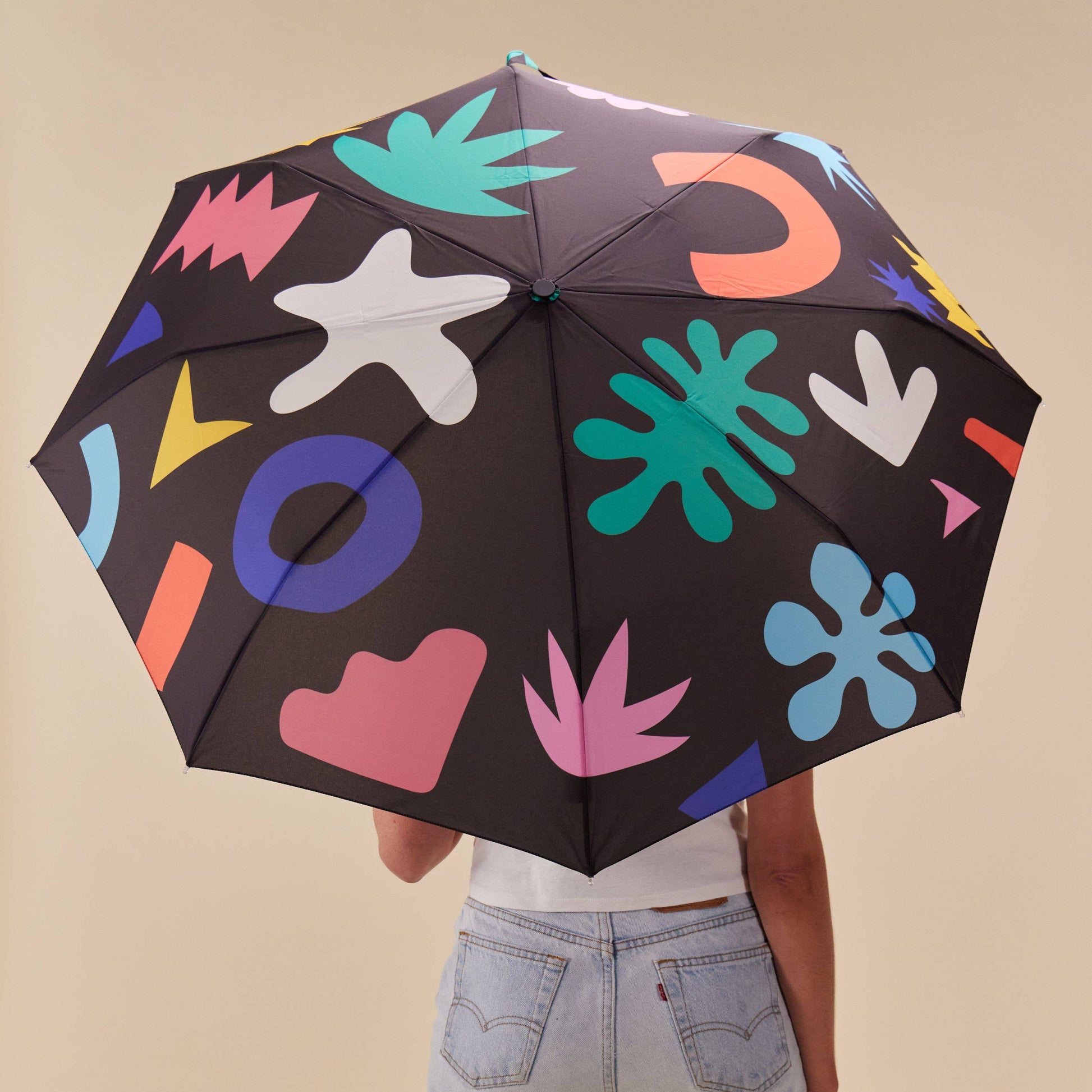 Person holding a black umbrella with colorful abstract patterns on a beige background