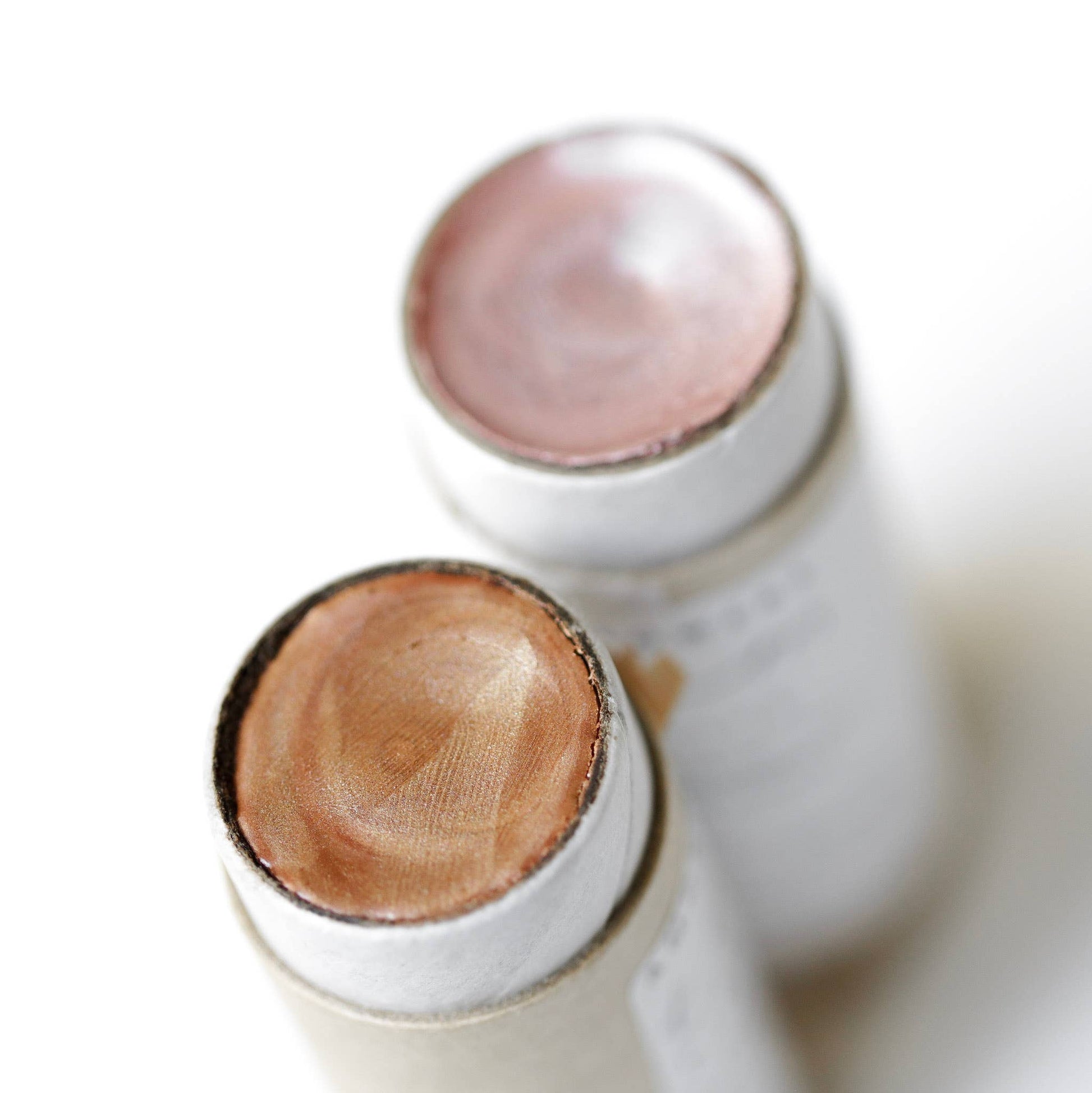 Two cylindrical containers with wooden and pinkish tops on a white background