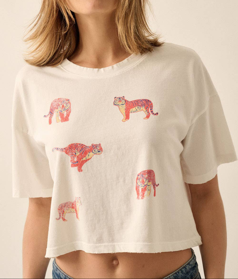 A woman wearing a cropped off-white t-shirt with a pattern of colorful leopard prints, set against a plain beige background.