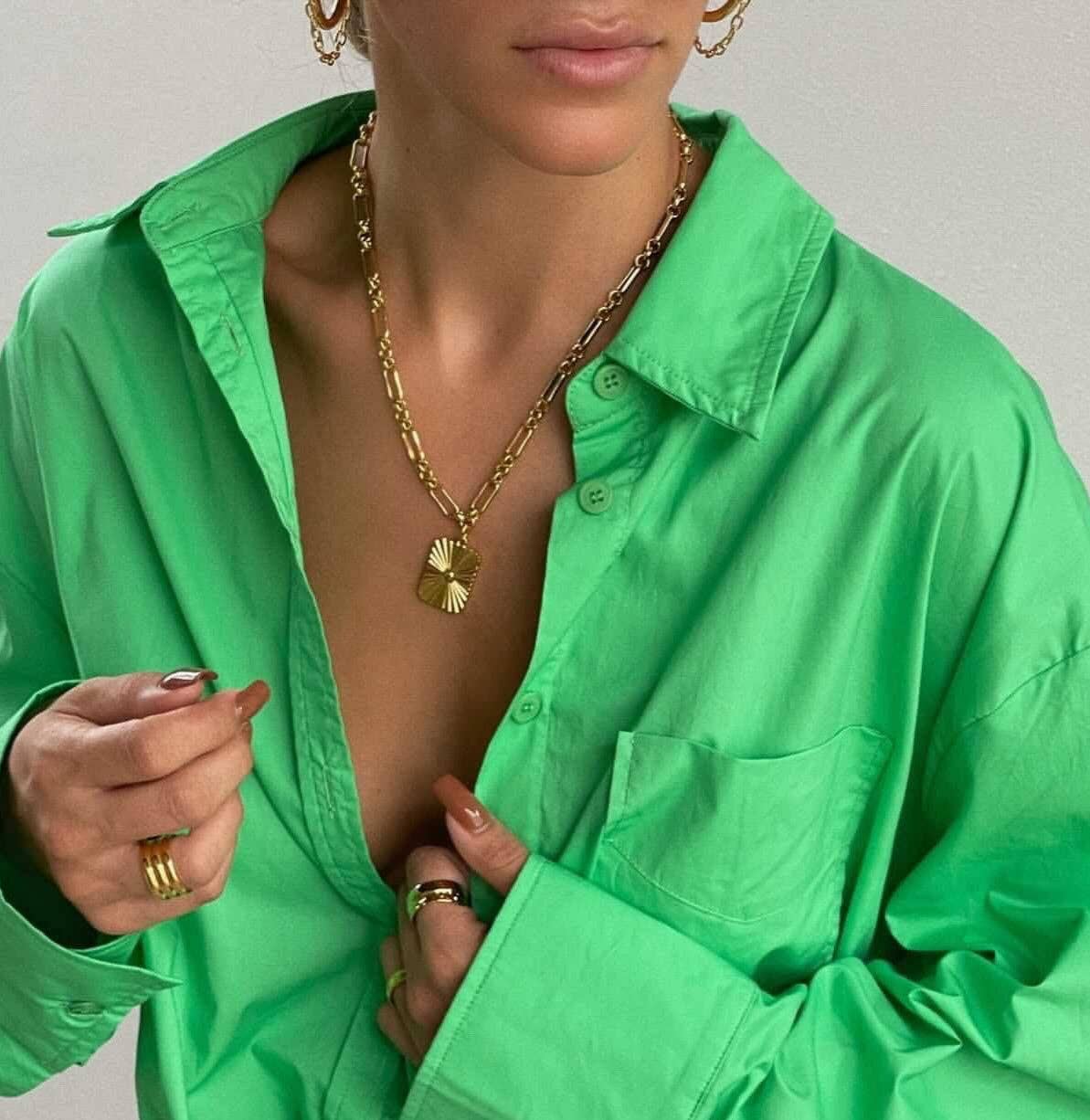 Person wearing a green button down shirt with a gold pendant necklace