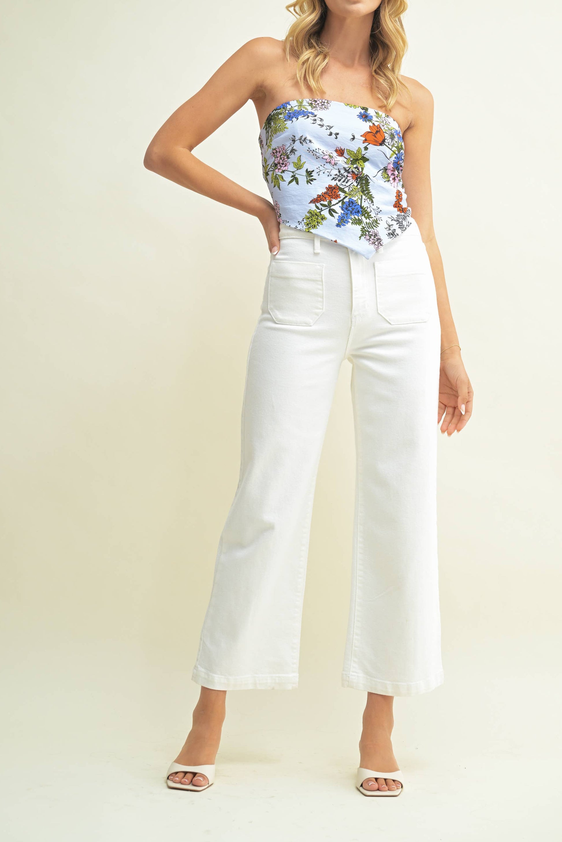 Woman wearing a floral strapless top and white pants on a plain background