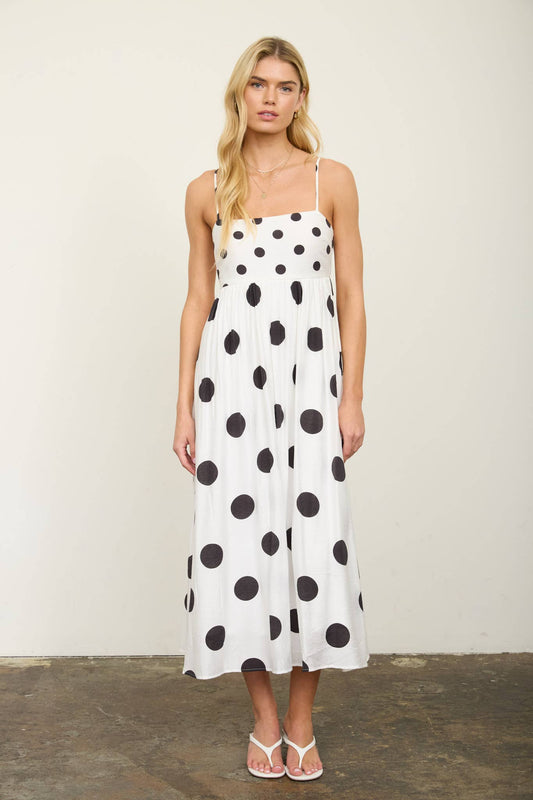 Woman wearing a white dress with black polka dots against a plain background