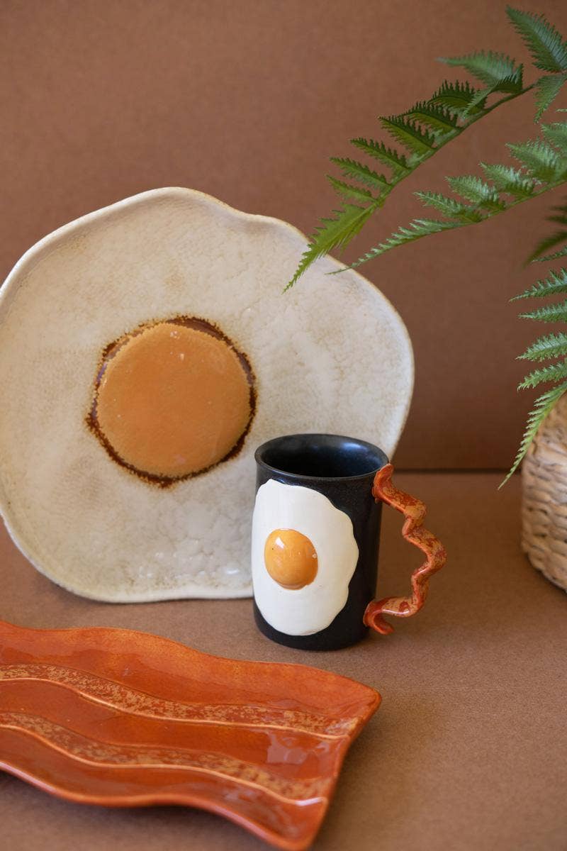 Ceramic mug with an egg design on a brown surface with decorative elements.