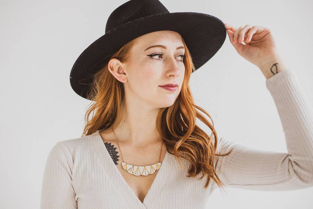 Woman wearing a black hat and beige sweater with a white background