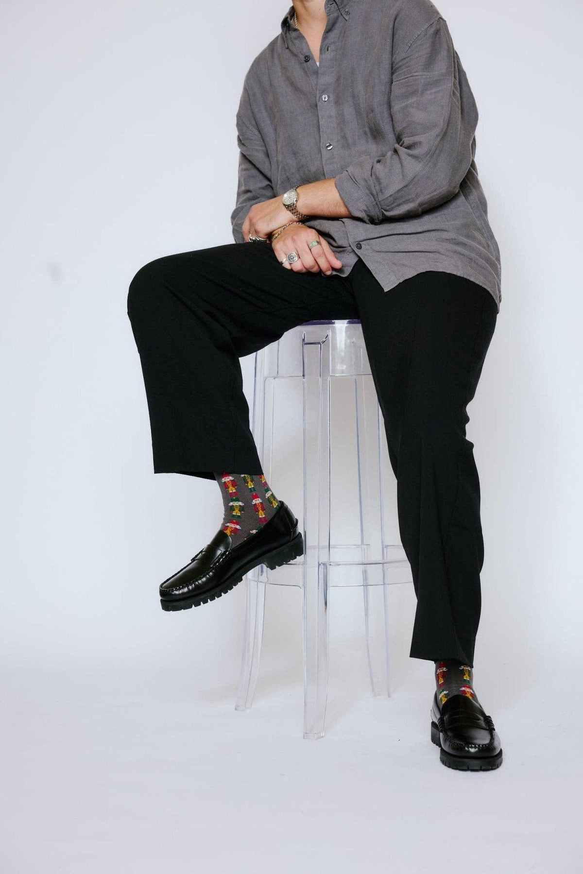 Person sitting on a transparent stool wearing a gray shirt, black pants, and patterned socks.
