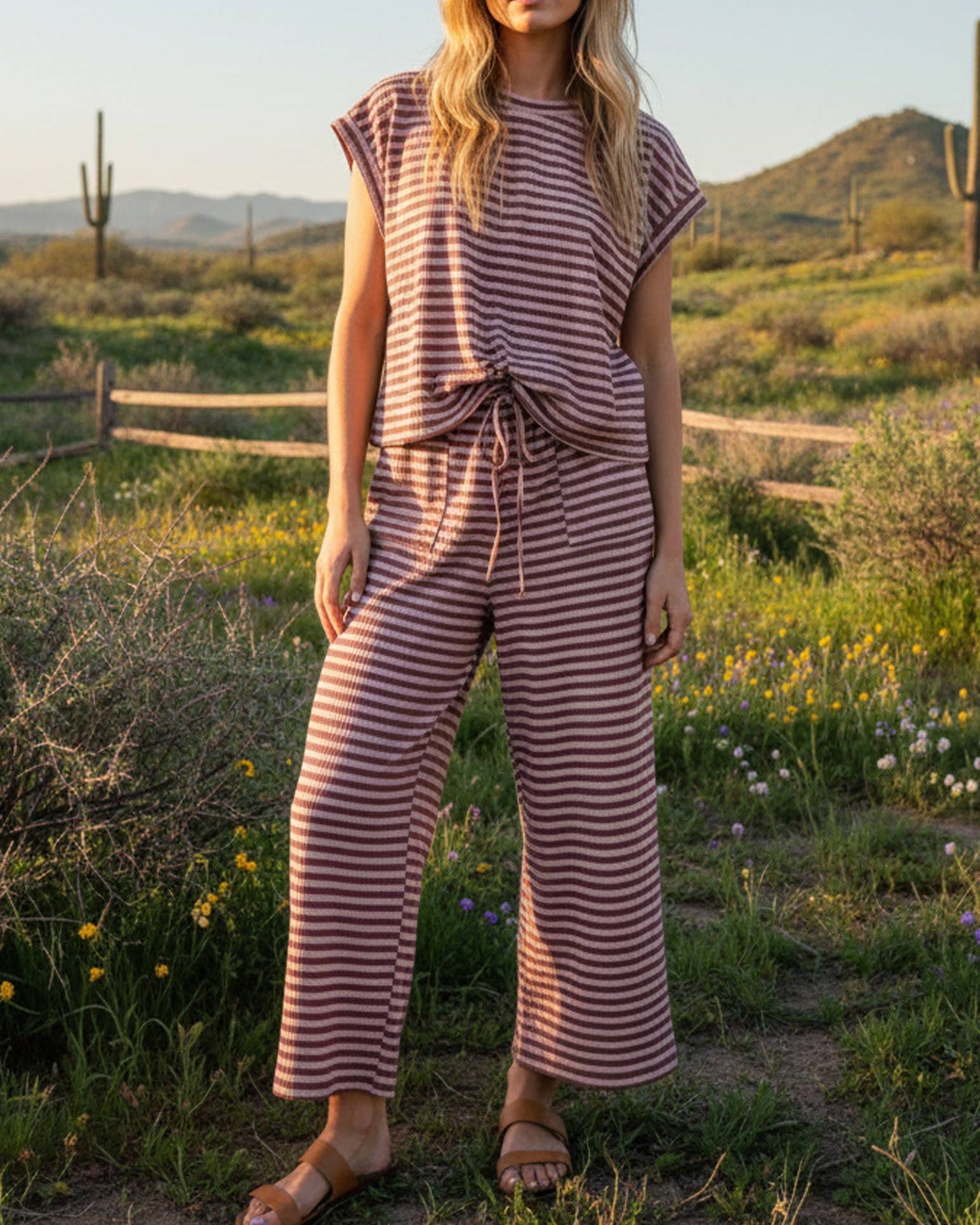 Woman in a striped outfit standing in a desert landscape with mountains in the background.